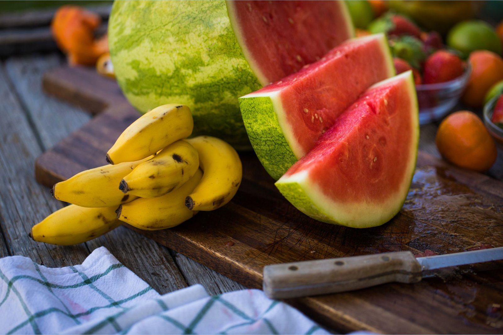 A káliumban gazdag banán egy L-citrullinban gazdag, szeletelt görögdinnye mellett fekszik a vágódeszkán.